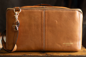 Brown leather bag with a strap on a wooden surface