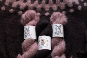 Three skeins of yarn with labels on a textured fabric background