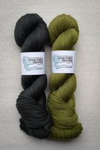 Load image into Gallery viewer, Two skeins of yarn, one black and one green, with labels on a neutral background