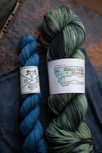 Load image into Gallery viewer, Two skeins of yarn, one blue and one green, with labels on a textured surface.