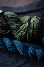 Load image into Gallery viewer, Three skeins of yarn in green and blue tones on a dark fabric background