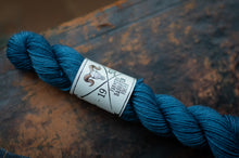 Load image into Gallery viewer, Blue skein of yarn with a label on a wooden surface