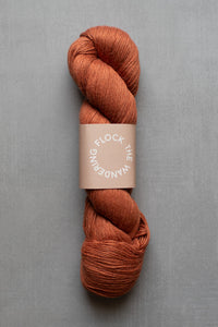 Skein of rust-colored yarn with a label on a gray background