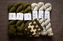 Load image into Gallery viewer, Three skeins of green yarn and two skeins of beige yarn with a knitted swatch on a brown background.