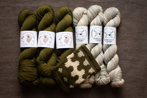 Three skeins of green yarn and two skeins of beige yarn with a knitted swatch on a brown background.