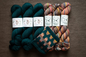 Three skeins of yarn in teal and multicolor with a knitted swatch on a brown background.