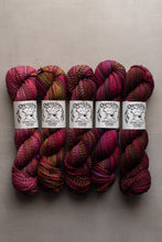 Load image into Gallery viewer, Five skeins of variegated yarn from Dream Catcher Specialty Yarn arranged side by side on a neutral gray background. The yarn features a marbled pattern of deep magenta, burgundy, purple, and hints of green and gold.