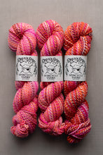 Load image into Gallery viewer, Three skeins of variegated yarn from Dreamy States Yarns arranged side by side on a neutral gray background. The yarn features a variegated pattern of pink, orange, red, and white, with white paper labels wrapped around the center of each skein.