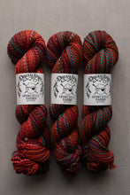 Load image into Gallery viewer, Three skeins of variegated yarn from Dreamy Sheep Spincycle Yarns arranged side-by-side on a neutral gray background. The yarn features a variegated pattern of red, orange, and dark blue.