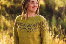 Load image into Gallery viewer, A woman wearing a knitted sweater in an outdoor setting with warm, golden sunlight filtering through trees. The sweater is a muted olive green with a dark brown Fair Isle pattern across the chest.