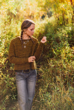 Load image into Gallery viewer, A woman with her hair in a braid stands in a sunlit outdoor field wearing a textured olive-brown knit sweater, gray jeans, and layered necklaces.