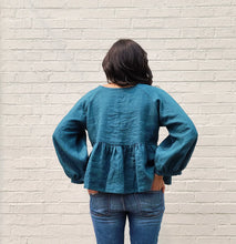 Load image into Gallery viewer, Person wearing a blue blouse with puffed sleeves against a light gray brick wall.