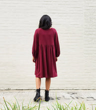 Load image into Gallery viewer, Person wearing a burgundy dress standing against a white brick wall.