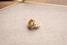 Load image into Gallery viewer, Two gold rings with floral designs on a textured beige surface