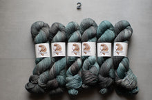Load image into Gallery viewer, skeins of variegated yarn laid side by side on a light gray surface, with a small number 2 printed above them. The yarn has a variegated colorway shifting between teal, slate blue, and charcoal gray.