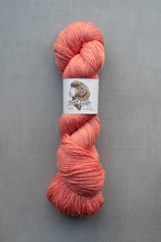 Load image into Gallery viewer, Peach-colored skein of yarn with a label on a gray background
