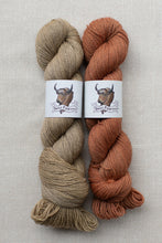 Load image into Gallery viewer, Two skeins of yarn side by side on a neutral textured background. The left skein is a warm sandy beige with a white paper label featuring a bison illustration and the text 'Best Paw Fleece'.