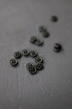 Load image into Gallery viewer, Small black buttons scattered on a gray surface