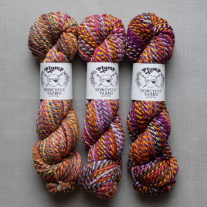 Three skeins of multicolored yarn with 'Plump Spincycle Yarns' labels on a gray background