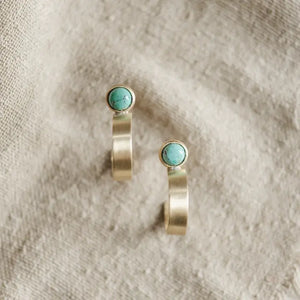 Pair of gold earrings with turquoise stones on a textured beige background