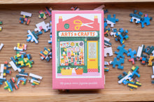 Load image into Gallery viewer, Pink &#39;Arts &amp; Crafts&#39; mini jigsaw puzzle box with scattered puzzle pieces on a wooden surface.