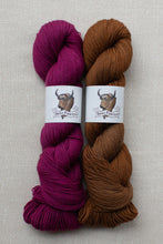 Load image into Gallery viewer, Two skeins of yarn side by side on a light beige textured fabric background. The left skein is a rich magenta-purple, and the right skein is a warm medium brown.