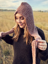 Load image into Gallery viewer, A woman wearing a chunky ribbed knit hooded scarf in a dusty rose and mauve color, standing in an open grassy field.