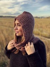 Load image into Gallery viewer, A woman wearing a chunky knit hooded cowl in a dusty mauve-brown color, standing in an outdoor field.