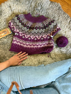 Knitted sweater with a pattern on a fluffy surface, accompanied by a ball of yarn.