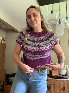 Woman wearing a purple patterned top and blue jeans indoors.