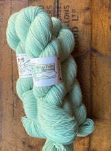 Load image into Gallery viewer, Light green skein of yarn with a label on a wooden background