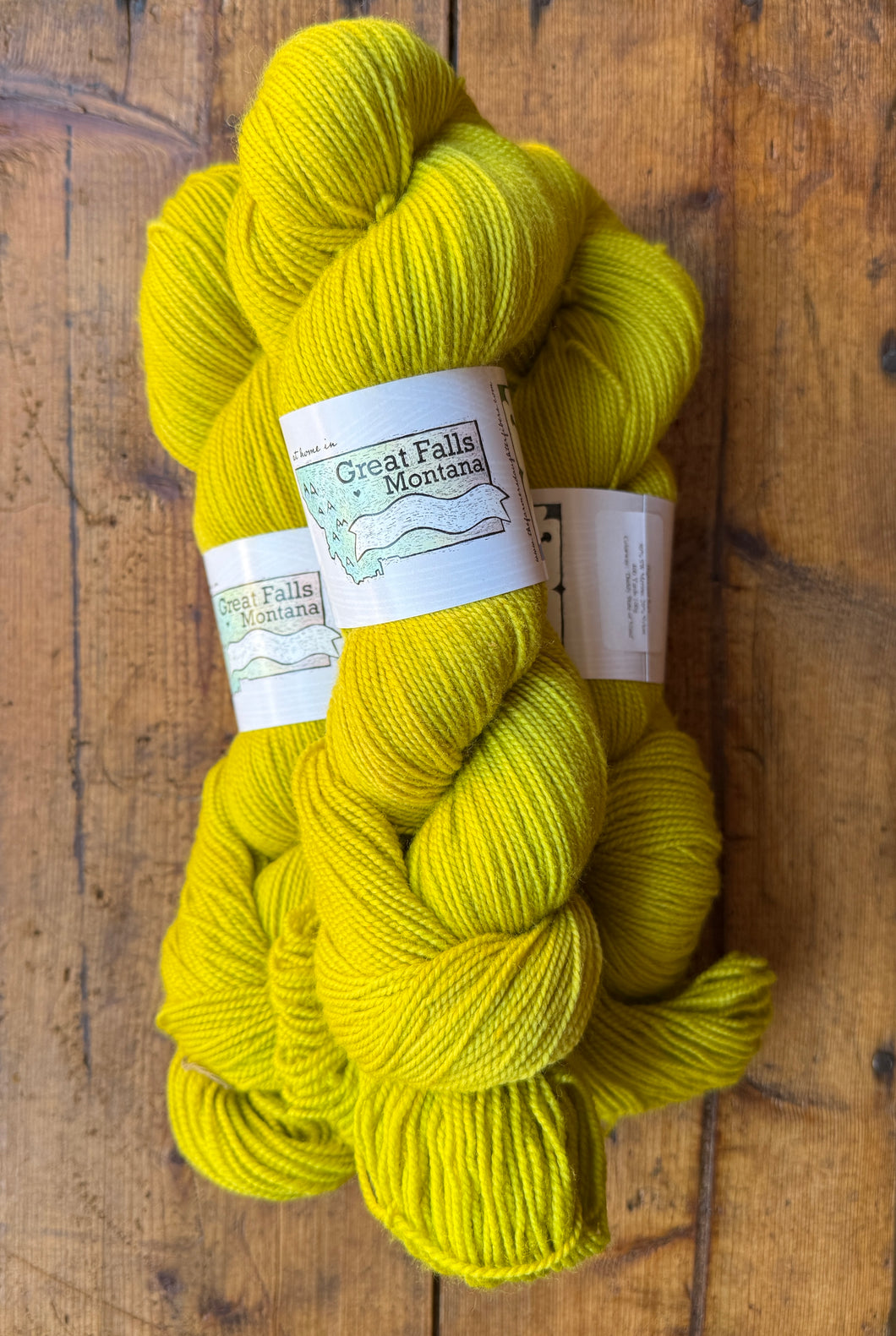 Three skeins of bright yellow yarn with a label on a wooden surface