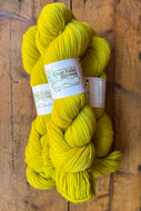 Three skeins of bright yellow yarn with a label on a wooden surface