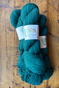 Three skeins of teal yarn with labels on a wooden surface
