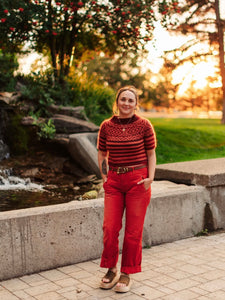 Person wearing a red sweater and pants standing in a park with trees and water features.