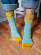 Person wearing light blue socks with yellow accents on a wooden floor.