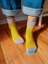 Load image into Gallery viewer, Person wearing yellow socks with purple accents on a wooden floor.