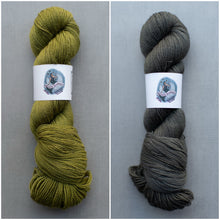Load image into Gallery viewer, Two skeins of yarn, one green and one gray, on a gray background with labels.