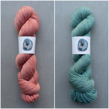 Load image into Gallery viewer, Two skeins of yarn, one pink and one green, on a gray background with a brand label.