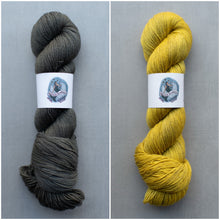 Load image into Gallery viewer, Two skeins of yarn, one gray and one yellow, on a gray background with labels.