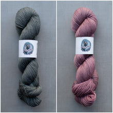 Load image into Gallery viewer, Two skeins of yarn, one gray and one pink, on a gray background with a brand label.