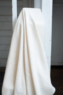 White textured fabric draped over a white ladder against a neutral background