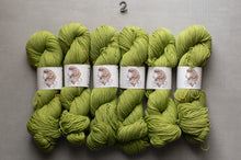 Load image into Gallery viewer, Green yarn skeins with labels on a gray background