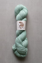 Load image into Gallery viewer, Skein of green yarn with a label on a gray background