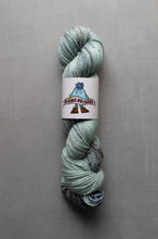 Load image into Gallery viewer, Skein of green yarn with a label on a gray background