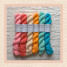 Load image into Gallery viewer, Five skeins of colorful yarn in pink, red, orange, beige, and blue on a textured surface with 'The Yarn Market' labels.