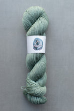 Load image into Gallery viewer, Skein of green yarn with a label on a gray background