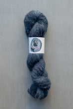 Load image into Gallery viewer, A skein of dark blue-gray wool yarn with a white paper label in the center, photographed against a neutral gray textured background.