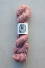 Load image into Gallery viewer, A skein of fluffy, twisted wool yarn in a dusty rose pink color, featuring a white paper label with a blue circular logo that reads 'non-traditional'. The yarn is photographed vertically against a neutral, textured gray background.