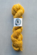 Load image into Gallery viewer, A skein of fluffy golden-yellow yarn wrapped with a white paper label featuring a blue circular logo, set against a plain gray background.